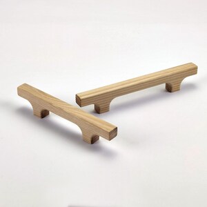 Puede incluir: Dos tiradores de armario de madera con acabado natural. Cada tirador es rectangular con un dise&ntilde;o curvo en los extremos. Los tiradores miden aproximadamente 15 cm de largo.