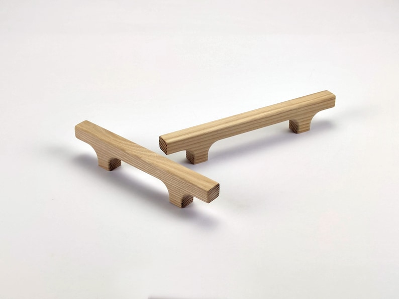 Puede incluir: Dos tiradores de armario de madera con acabado natural. Cada tirador es rectangular con un dise&ntilde;o curvo en los extremos. Los tiradores miden aproximadamente 15 cm de largo.
