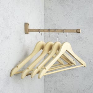 Könnte beinhalten: Ein hölzerner Kleiderständer mit fünf hellfarbigen Holzkleiderbügeln. Der Ständer ist an einer hellgrauen Wand montiert. Die Kleiderbügel hängen an einer Metallstange.