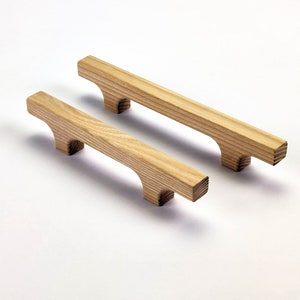 Puede incluir: Dos tiradores de armario de madera con acabado natural. Los tiradores son rectangulares con un dise&ntilde;o de asa curvada. La veta de la madera es visible y los tiradores son de color marr&oacute;n claro. Adecuado para armarios de cocina o ba&ntilde;o.