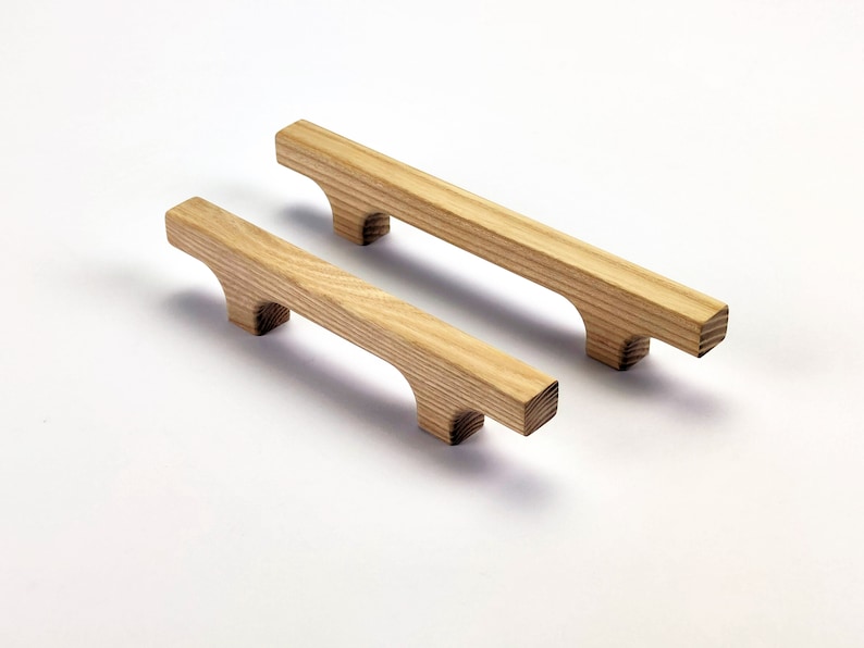 Puede incluir: Dos tiradores de armario de madera con acabado natural. Los tiradores son rectangulares con un dise&ntilde;o de asa curvada. La veta de la madera es visible y los tiradores son de color marr&oacute;n claro. Adecuado para armarios de cocina o ba&ntilde;o.