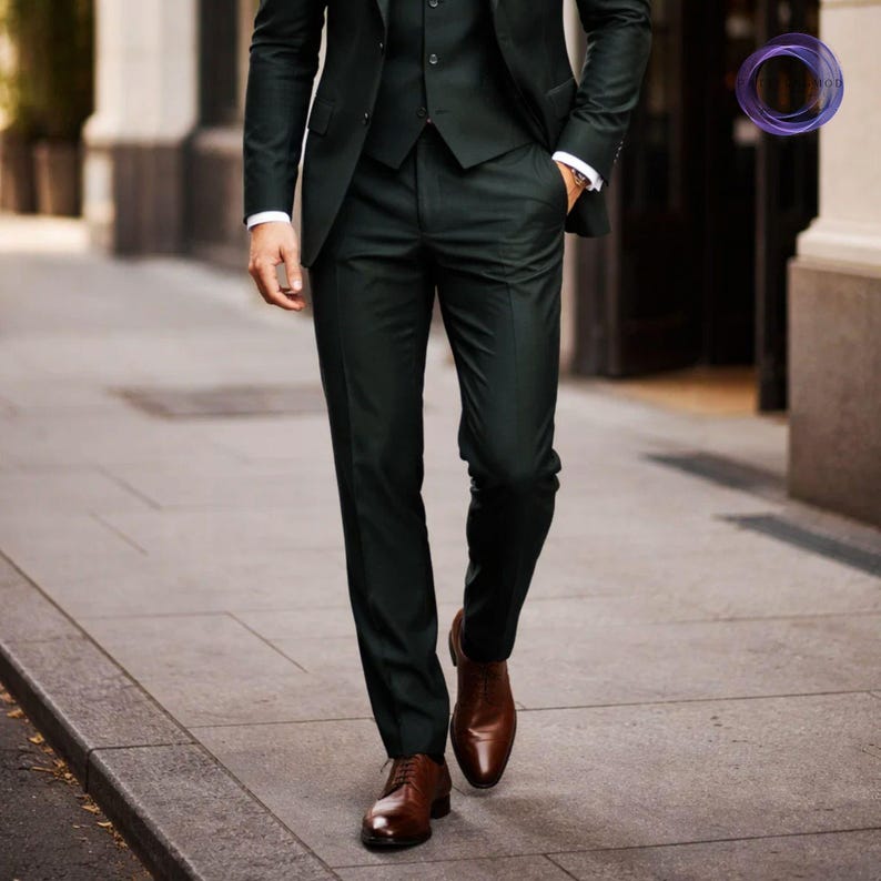 May include: A three-piece dark green suit with a matching jacket, vest, and trousers. The suit is paired with a white dress shirt and brown leather shoes. The image shows a person walking on a sidewalk.