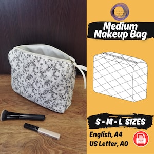Puede incluir: Un neceser con estampado floral blanco con cierre de cremallera y tirador de cinta blanca. La bolsa está abierta, revelando un interior blanco. Un pincel de maquillaje y un corrector están al lado de la bolsa. El texto "Medium Makeup Bag" es visible.