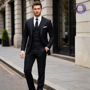 May include: A three-piece black suit with a white dress shirt and black tie. The suit includes a jacket, vest, and trousers. The man is standing on a sidewalk in front of a building.