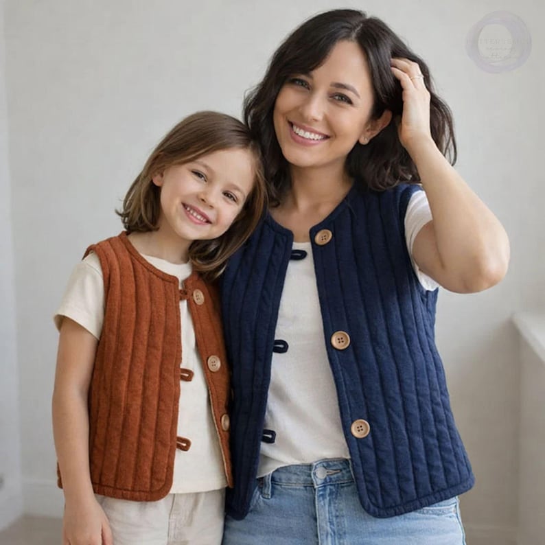 May include: Two people wearing quilted vests. One vest is a rust color, the other is navy blue. Both vests have wooden buttons and a vertical quilted pattern. They are wearing white t-shirts underneath.