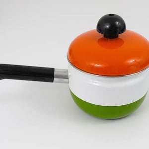 Può includere: Un piccolo pentolino con corpo bianco e verde, dotato di un coperchio arancione brillante sormontato da un pomello nero. Il pentolino ha un lungo manico nero dritto fissato a una base in metallo argentato, offrendo una vista chiara.