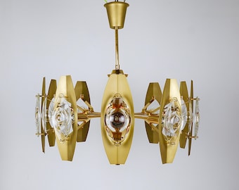May include: A mid-century modern chandelier with a gold finish. The fixture features multiple oval-shaped elements with clear glass accents and a central light source. The design is symmetrical and geometric, suitable for interior lighting.