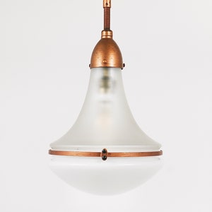 May include: A frosted glass pendant light with a copper finish and a decorative band around the middle. The light is hanging from a copper chain.