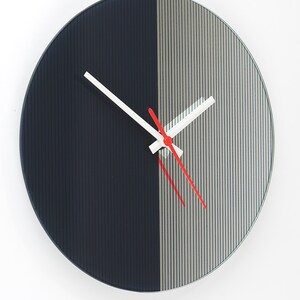 May include: A modern wall clock with a minimalist design. The clock face is divided into two vertical sections: one in dark navy blue and the other in silver with vertical lines. The hands are white with a red second hand.