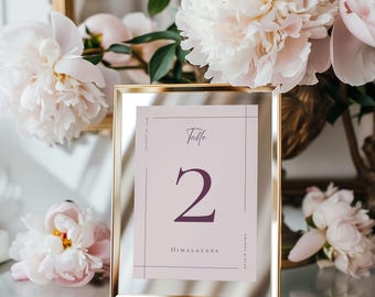 May include: A gold framed table number card with a pink background. The number "2" is printed in a dark purple color. The text "Table" and "HIMALAYANS" are printed in a light purple color.