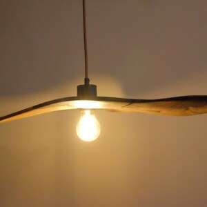 May include: A wooden, propeller-shaped pendant light fixture. The light fixture has a warm, natural wood finish and a single exposed light bulb. The fixture hangs from a thin cord, casting a warm glow.