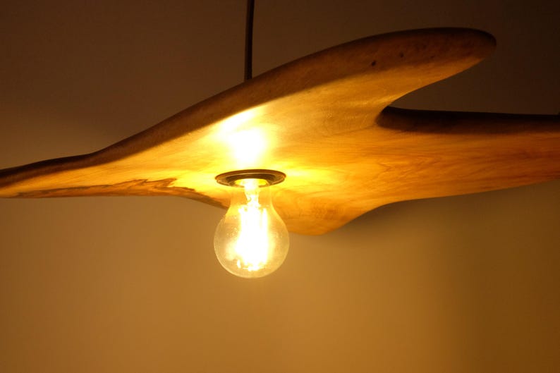 May include: A wooden, organic-shaped pendant light fixture with a warm, glowing light bulb. The fixture is made of light-colored wood and hangs from a dark cord. The bulb is a classic Edison style.