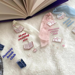 Peut inclure: Quatre marque-pages transparents avec des illustrations et des textes sur le thème du livre. Les motifs comprennent "fantasy book club", "in my reading era", "romance reader club" et "just one more chapter".