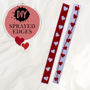 Peut inclure: Deux bandes de papier blanc avec des cœurs rouges découpés. Les bandes sont étiquetées "DIY SPRAYED EDGES".