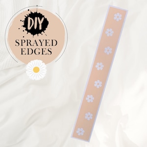 Peut inclure: Une longue bande de papier beige avec une bordure blanche et un motif répétitif de marguerites blanches. Le texte "DIY SPRAYED EDGES" est visible en arrière-plan.
