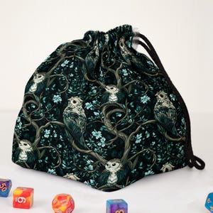 May include: A drawstring bag with a dark teal background featuring a repeating pattern of owls perched on tree branches with light blue flowers. The bag has a black drawstring closure.