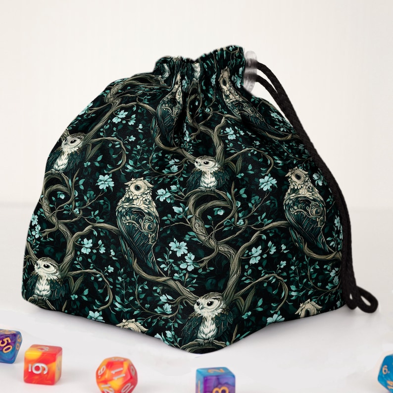 May include: A drawstring bag with a dark teal background featuring a repeating pattern of owls perched on tree branches with light blue flowers. The bag has a black drawstring closure.