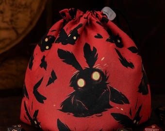 May include: Red drawstring dice bag with a black creature design and yellow eyes. The bag features a repeating pattern of the creature and other shapes. Several dice are visible near the bag.