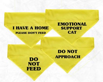 May include: Four yellow triangular bandanas with black text. The bandanas read: "I HAVE A HOME PLEASE DON'T FEED", "EMOTIONAL SUPPORT CAT", "DO NOT FEED", and "DO NOT APPROACH".