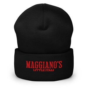 May include: Black beanie with the red text "Maggiano's Little Italy" embroidered on the cuff. The beanie is made of a soft, knitted material. The hat is a winter accessory.