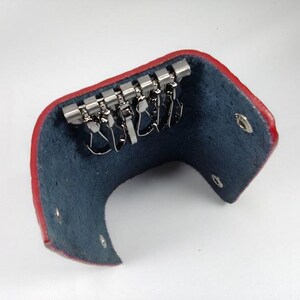 Puede incluir: Porta llaves de cuero rojo con interior azul y un llavero de metal con varios ganchos.