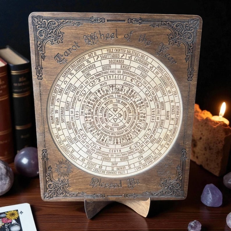 Może przedstawiać: Drewniane Koło Tarota Roku, z okrągłym wzorem z symbolami astrologicznymi i tekstem. Drewniana rama ma dekoracyjne rzeźbienia. Koło jest wyświetlane na drewnianym stojaku. Tekst zawiera "Blessed Be".