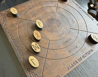 May include: A wooden divination board with engraved Celtic knot designs and circular zones labeled "Past," "Present," and "Future." Includes wooden rune stones. The board is dark brown with lighter-colored engraved text and symbols.
