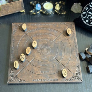 K&ouml;nnte beinhalten: Ein dunkelbraunes Holz-Divinationsbrett mit eingravierten keltischen Knotenmustern und Runensymbolen. Das Brett hat konzentrische Kreise und Text, mit h&ouml;lzernen Runensteinen, die darum verstreut sind. Ein schwarzer Beutel und andere mystische Gegenst&auml;nde sind im Hintergrund.