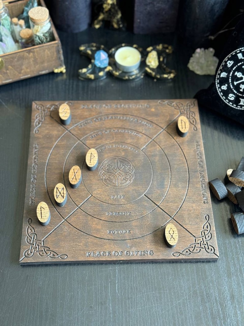 K&ouml;nnte beinhalten: Ein dunkelbraunes Holz-Divinationsbrett mit eingravierten keltischen Knotenmustern und Runensymbolen. Das Brett hat konzentrische Kreise und Text, mit h&ouml;lzernen Runensteinen, die darum verstreut sind. Ein schwarzer Beutel und andere mystische Gegenst&auml;nde sind im Hintergrund.