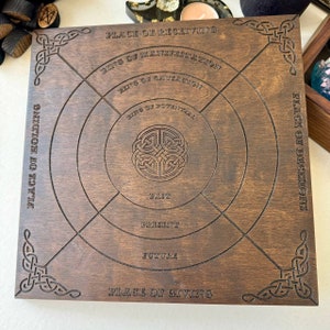 K&ouml;nnte beinhalten: Ein quadratisches Wahrsagebrett aus dunklem Holz. Das Brett zeigt gravierte Texte und kreisf&ouml;rmige Designs, darunter die Worte "Place of Receiving", "Ring of Manifestation" und "Past, Present, Future". Auf den Ecken und in der Mitte befinden sich keltische Knotenmuster.