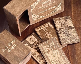 May include: A wooden tarot card deck and matching sliding box. The box lid is engraved with "TAROT RIDER-WAITE-SMITH TAROT ORIGINAL, 1910 22 MAJOR ARCANA". The cards feature engraved illustrations including Temperance, Justice, and The Hanged Man.