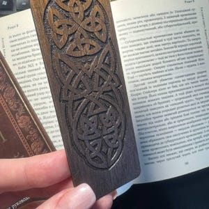 Pu&ograve; includere: Segnalibro in legno marrone scuro con design a nodo celtico intagliato. Il segnalibro &egrave; rettangolare con bordi arrotondati ed &egrave; posto sopra un libro aperto.