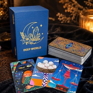Puede incluir: Una caja rectangular azul con gráficos en lámina dorada de una luna creciente, cristales y flores, etiquetada DEEP WORLD. Junto a ella hay una baraja con un diseño de ojo y tres cartas ilustradas que muestran un gato, un nido y una balanza.