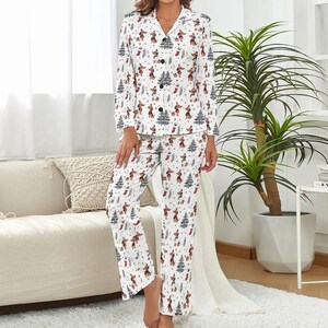 May include: White pyjama set featuring a festive pattern of dachshunds, Christmas trees, and stockings. The long-sleeved top has a button-down front and a notched collar. The trousers are straight-legged. The pyjamas are made of a soft, comfortable material.