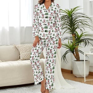 May include: White pajama set featuring a repeating pattern of dogs wearing red bandanas and green Christmas trees. The long-sleeved top has a collared neckline and button closure. The matching pants have a relaxed fit, perfect for lounging.