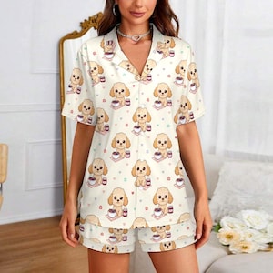 May include: Cream-colored pajama set featuring a repeating pattern of cartoon poodles with coffee cups and hearts. The short-sleeved button-down shirt and matching shorts are made of a soft fabric. The pajamas are a comfortable sleepwear option.