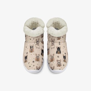 May include: A pair of beige indoor slippers with a repeating pattern of French bulldogs holding coffee cups. The slippers have a white sole and a fluffy, cream-colored lining around the ankle.