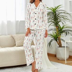 Op de afbeelding: Witte pyjamaset met een champagneglasprint. De top met lange mouwen heeft een knoopsluiting en een reverskraag. De bijpassende broek heeft een relaxte pasvorm. De champagneglazen zijn versierd met kerstmutsen en sterren.