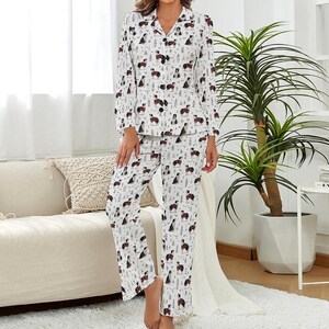 May include: White pajama set with a repeating pattern of black and brown dogs wearing red plaid scarves. The long-sleeved top has a collared neckline and button closure. The matching pants have a relaxed fit.