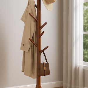 May include: A brown wooden coat rack with multiple pegs for hanging items. A tan coat, a beige hat, and a brown purse are displayed on the rack. The rack has a tripod base and is set against a neutral wall.