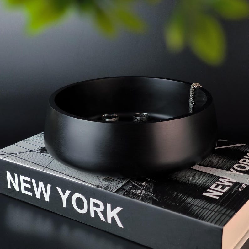 May include: A black eco-composite bowl with a smooth, glossy finish. The bowl is filled with small silver rings and a silver chain.