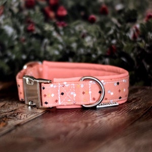 May include: A pink dog collar with a geometric pattern and silver hardware. The collar has a buckle closure and a D-ring for attaching a leash. The collar is made by Caniclix.