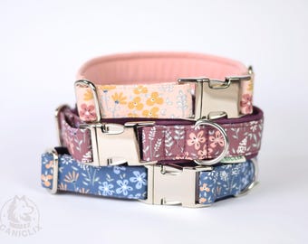May include: Three stacked dog collars with floral patterns. The top collar is pink with yellow flowers, the middle is purple with white flowers, and the bottom is blue with white flowers. Each collar has a silver buckle.