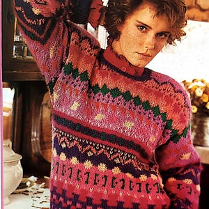 May include: A pink, green and purple patterned sweater with a crew neck. The sweater has a fair isle design with a variety of colours and textures.