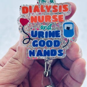 May include: A clear glitter badge holder with a white background and the text "I'm a Dialysis Nurse and Urine Good Hands". The badge holder has a blue and white IV bag graphic and a red heart balloon graphic. The badge holder is attached to a clear retractable badge reel.