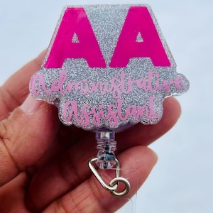 May include: A silver glitter badge holder with a pink "AA" and the text "Administrative Assistant". The badge holder is attached to a clear retractable badge reel.