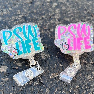 May include: Two badge reels with the text "PSW LIFE". One reel has teal lettering, the other has pink lettering. Both have a stethoscope graphic and glitter accents. Each reel has a clear plastic clip.