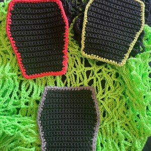 May include: Three crocheted black squares with different coloured borders. The squares have a slightly rounded rectangular shape. The borders are red, yellow, and grey.
