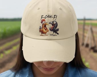 May include: Beige baseball cap with a distressed brim. The cap features a cartoon graphic of a chicken and a crow, with the text "F-CAW-F!" above them. The background shows a field.