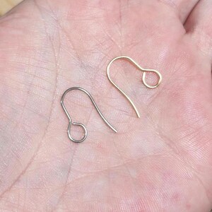 Op de afbeelding: Twee oorhaken, een zilveren en een gouden, worden getoond op een hand. De haken zijn beide open en klaar voor gebruik.